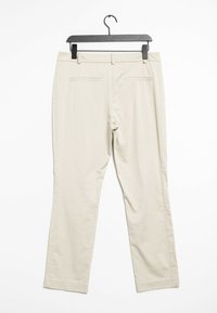 Pantalon beige avec une texture lisse, design à jambes droites et poches arrière doubles. Suspendu à un cintre en plastique noir.