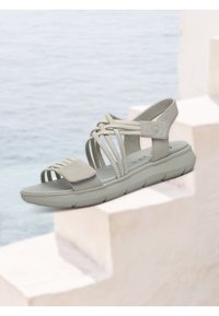 Sandalina grigio chiaro con cinturini intrecciati e suola imbottita. Presenta un cinturino alla caviglia sicuro e un'apertura ampia per le dita. Accenti testurizzati migliorano la presa.