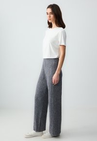 Witte t-shirt met korte mouwen, gecombineerd met grijze, gestructureerde, wijde broek met verticale ribbels en witte sneakers.