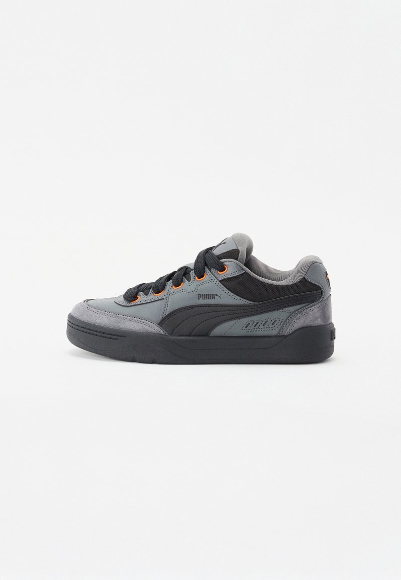 Zapatilla Puma en gris y negro con cordones negros, ojales naranja y una suela gruesa negra, mostrada en vista de perfil lateral.