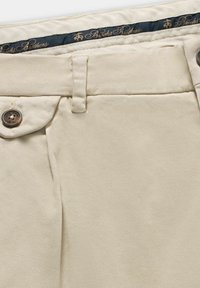 Beżowe bawełniane spodnie chino o gładkiej fakturze, z płaskim przodem i kieszeniami bocznymi. Posiadają zapięcie na guzik oraz ciemny pasek w talii z logotypem.
