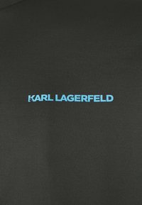 Tecido preto com uma textura suave apresentando o texto "KARL LAGERFELD" em letras bold, azuis claras, posicionadas centralmente.