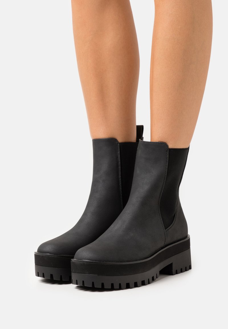 Black ankle boots made of smooth leather with elastic side panels and a chunky rubber sole featuring a pronounced tread pattern.