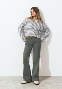 Striped long-sleeve shirt in gray and white, relaxed fit. Olive green flared pants with visible stitching, paired with beige low-top shoes.