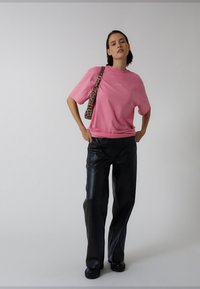 Rosa bomullst-shirt med avslappnad passform. Kombinerad med svarta vida byxor i konstläder. En leopardmönstrad handväska bärs över axeln.