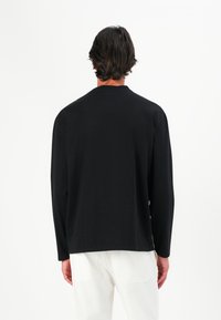 Zwarte langemouwenshirt met een ronde hals, gemaakt van zachte stof. Heeft een relaxte pasvorm en een minimalistisch ontwerp zonder zichtbare patronen.