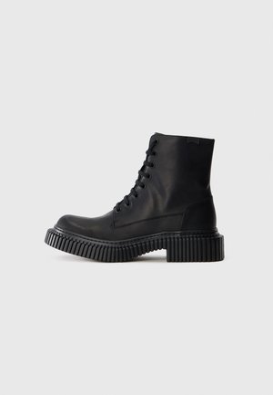 Botas de cuero negro hasta el tobillo con punta redonda, diseño de cordones y suela gruesa estriada. Textura suave con costuras mínimas y sin acentos visibles.
