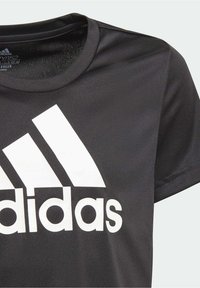 Camiseta deportiva negra hecha de una tela suave. Presenta un gran logo blanco de Adidas y tres franjas diagonales en el frente. Mangas cortas.