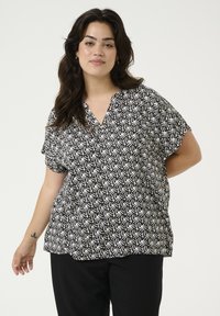 Blouse à manches courtes noire et blanche à motifs avec un décolleté en V, offrant une coupe ample et un tissu doux.