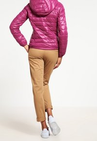 Lśniąca fuksjowa kurtka puchowa z kapturem, z pikowanym wzorem. W połączeniu z podwiniętymi khaki spodniami i białymi sneakersami.