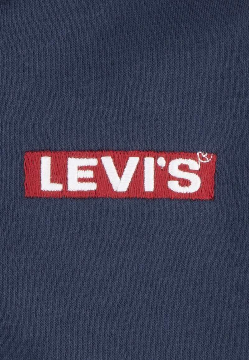 Dunkelblauem Stoff mit einem auffälligen roten rechteckigen Patch, auf dem in der Mitte der weiße gestickte Text "LEVI'S" steht. Glatte Textur.