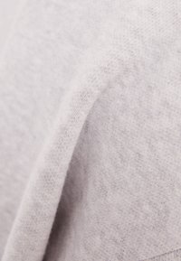 Suéter gris claro hecho de una tela suave y texturizada con una superficie ligeramente esponjosa. Presenta un diseño relajado y un ajuste drapeado.