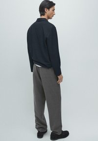 Czarny pulower z kołnierzem w zestawieniu z luźnymi szarymi spodniami. Strój uzupełniają czarne buty, podkreślające swobodny fason.