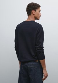 Navy blue knit sweater with long sleeves, ribbed cuffs, and a round neckline, paired with dark denim jeans, viewed from the back.