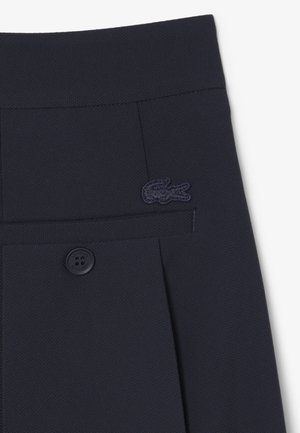 Shorts en tissu texturé bleu marine foncé avec une poche arrière boutonnée et un logo crocodile bleu marine foncé cousu au-dessus de la poche.