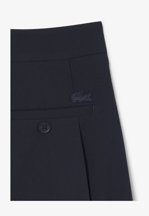 Pantalones cortos de tela texturizada azul marino oscuro con un bolsillo trasero con botón y un logo de cocodrilo azul marino oscuro bordado sobre el bolsillo.