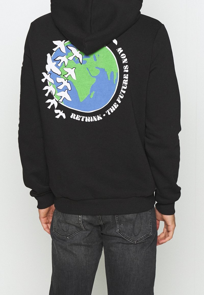 Sudadera negra con un gráfico de la Tierra en colores azul y verde, rodeada de siluetas de aviones blancos y el texto: "REPIENSA • EL FUTURO ES AHORA."