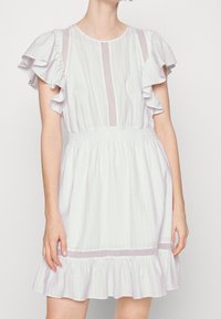 Vestido de lavanda claro con mangas cortas con volantes, cintura fruncida y un dobladillo con vuelo. Presenta rayas verticales y un sutil detalle de malla.