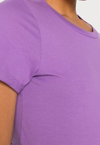Fialové bavlněné tričko s krátkými rukávy, které má kulatý výstřih a hladkou texturu. Střih se jeví jako blízký tělu.