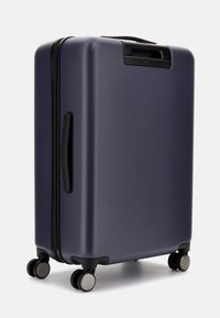 Valigia rigida viola con superficie liscia, manico nero e quattro ruote. Dotata di chiusura a zip e design rettangolare elegante.