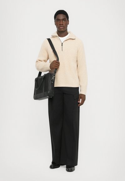 Ljus beige ribbad stickad zip-up tröja, svart axelväska, vida svarta byxor och svarta skor. Enkelt design med texturerad stickning och kontrasterande färger.