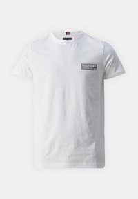 Bílý bavlněný tričko s kulatým výstřihem, krátkými rukávy a černým obdélníkovým logem na levé straně, které obsahuje "HILFIGER" a "ESTABLISHED 1985 USA."