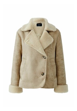 Beige Kunstschaffelljacke mit großem Kragen, doppelt geknöpftem Design, zwei vorderen Taschen und weicher Textur. Knopfdetails vorne.