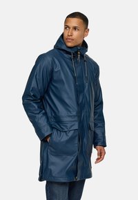Navy waterdichte parka met een capuchon, rits aan de voorkant, twee grote zakken en verstelbare koordjes. Gemaakt van een gladde, matte stof.