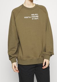 Felpa verde oliva con testo bianco "RILASSATI. CE LA FARAI." Maniche raglan e polsini e orlo a costine, realizzata in tessuto morbido.