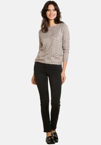 Beżowa bluzka z długim rękawem w wzór lamparta, zestawiona z czarnymi jeansami slim fit i czarnymi mokasynami. Gładka tekstura materiału.