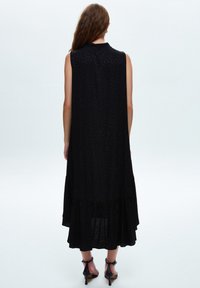 Svart ärmlös maxiklänning med en strukturerad mönster, har en lager-på-lager nederkant, tillverkad av lättviktsmaterial, lämplig för varmt väder.