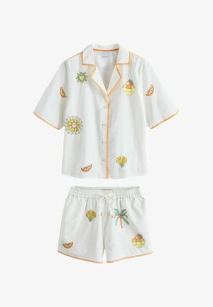 Biały lniany komplet piżamowy z krótkim rękawem i szortami. Ozdobiony kolorową haftowaną grafiką słońca, owoców i muszli; wykończenia w kolorze pomarańczowym.