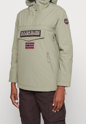 Lichtolijfgroene capuchonjas met ritssluiting aan de voorkant en zak, Napapijri-logo patch en Noorse vlag op de borst, gedragen met donkerbruine broek.