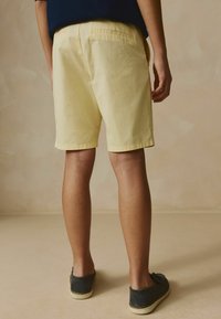 Gula bomullsshorts med rak passform, något ovanför knäet, har två bakfickor. Bärs med mörka slip-on skor.