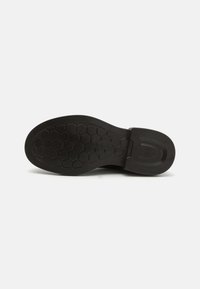 Suola di scarpa in gomma nera con un motivo a nido d'ape e una forma arrotondata; presenta un tacco piccolo e bordi lisci.
