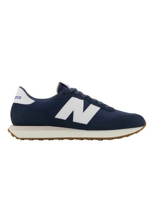 Scarpa da ginnastica sportiva blu navy e bianca con design stringato, suola beige spessa e grande logo "N" bianco sul lato.