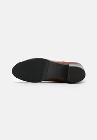Zapato de cuero marrón con un tacón bajo, con un acabado suave, punta redonda y una suela de goma negra con tracción estriada.
