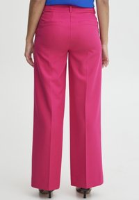 Fuchsia weit geschnittene Hose mit glatter Textur, mit Gesäßtaschen und tailliertem Bund. Getragen mit einem blauen Oberteil und schwarzen Absätzen.
