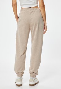 Beige strukturierte Jogginghosen mit elastischem Bund und Bündchen, ausgestattet mit Seitentaschen und einer lockeren Passform, kombiniert mit weißen Turnschuhen.
