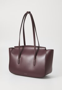Sac fourre-tout en cuir bordeaux avec une finition lisse, des poignées allongées et une forme structurée. Présente un design minimaliste avec un branding subtil.