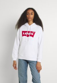 Felpa bianca in cotone con tasca a marsupio, caratterizzata da un grande logo rosso Levi's sulla parte frontale. Tessuto strutturato con coulisse regolabile.