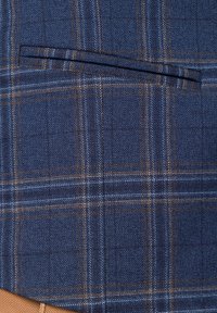 Materiał w kratę w kolorze granatowym z jasnoniebieskimi i brązowymi akcentami. Gładka struktura z detalem kieszeni na klatce piersiowej.