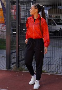 Sarkans, spīdīgs jaka ar baltu rāvējslēdzēju, kombinēta ar melnām sporta biksēm un baltām kedām. Jakai ir elastīgas piedurknes; sporta biksēm ir logotips.