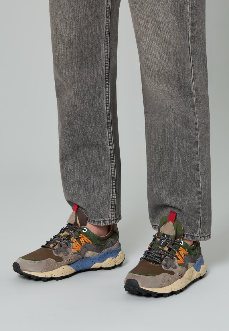 Mehrfarbige Sneakers, die eine Mischung aus braunen, grünen und blauen Materialien aufweisen, mit Wildlederstruktur und einer markanten Gummisohle mit ausgeprägten Stollen.