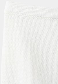 Gros plan d’un tissu tricoté blanc avec des coutures visibles le long du bord supérieur, montrant un motif de fil finement texturé.