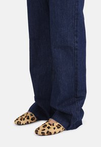 Ballet flat con punta a contrasto in pelliccia sintetica leopardata, abbinate a jeans in denim a gamba larga blu scuro. Dettagli includono orlo sfrangiato sui jeans.