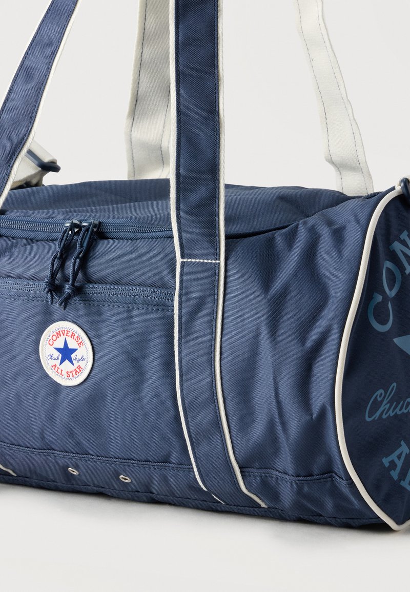 Marineblaue Converse Duffel-Tasche mit weißem Besatz, doppelten Griffen, Reißverschlusstasche und rundem "Converse All Star" Logo-Patch.
