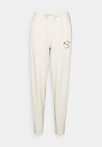 Cream-colored sweatpants with a drawstring waist, tapered leg, and side pockets. Features a circular graphic design on the left thigh.