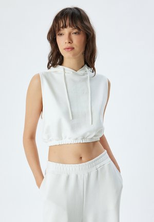 Sudadera blanca recortada con capucha ajustable. Presenta una tela suave y un dobladillo elástico. Combinada con pantalones relajados de color claro a juego.