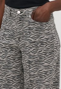 Gray zebra-print denim pants featuring a mid-rise waist, four pockets, and contrasting stitching, capturing a textured, animal-inspired design.